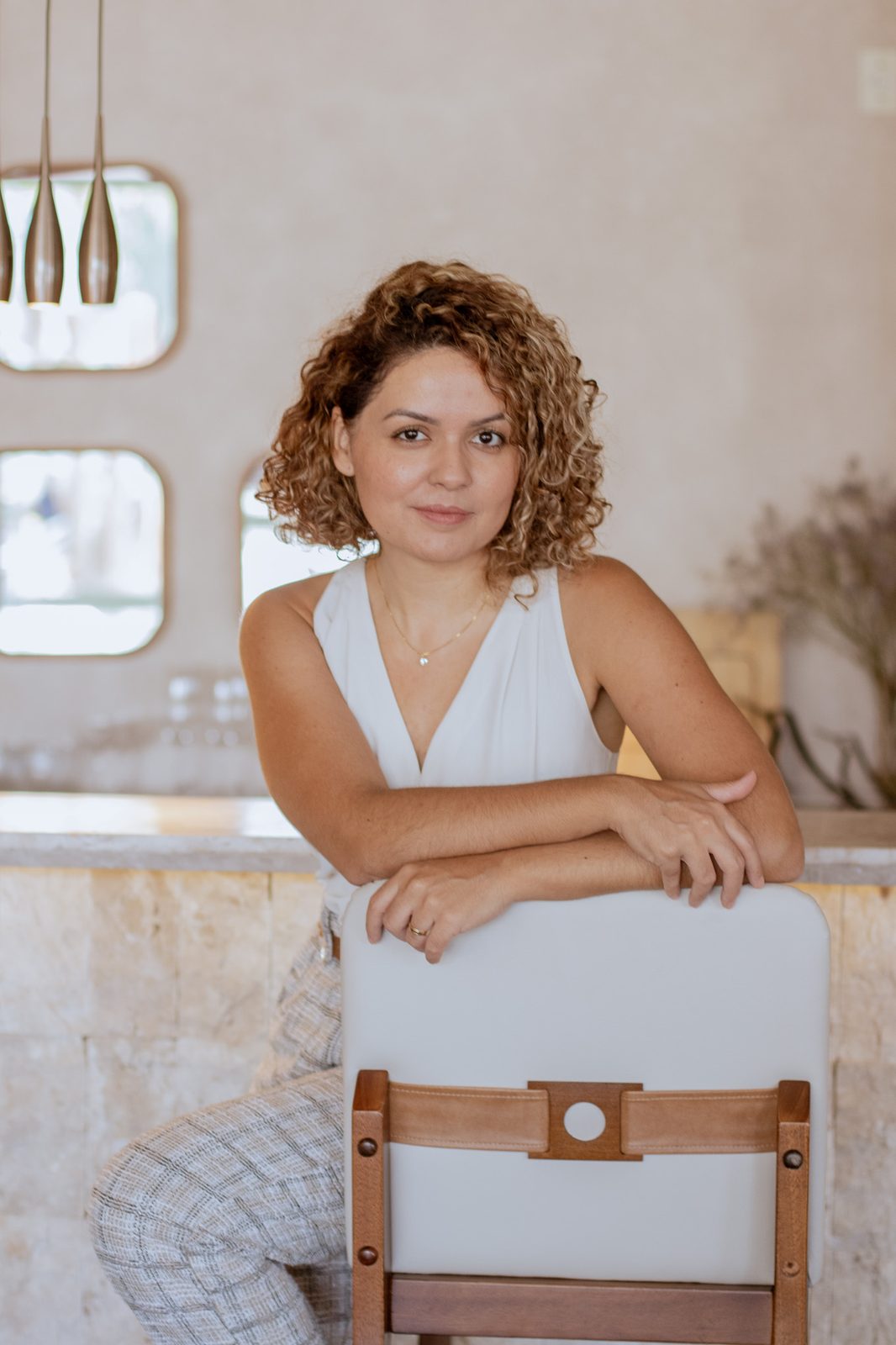 Thaís apoiada em uma cadeira, olhando para a câmera, em ambiente projetado por ela